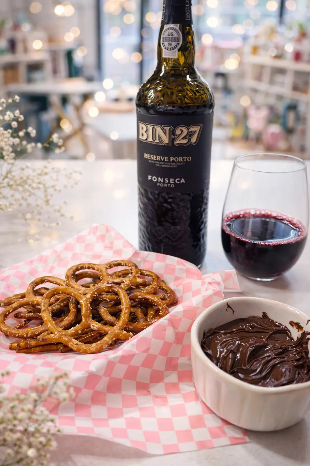 aesthetic picture of port wine in a glass, pretzels in a pink checkered basket and nutella