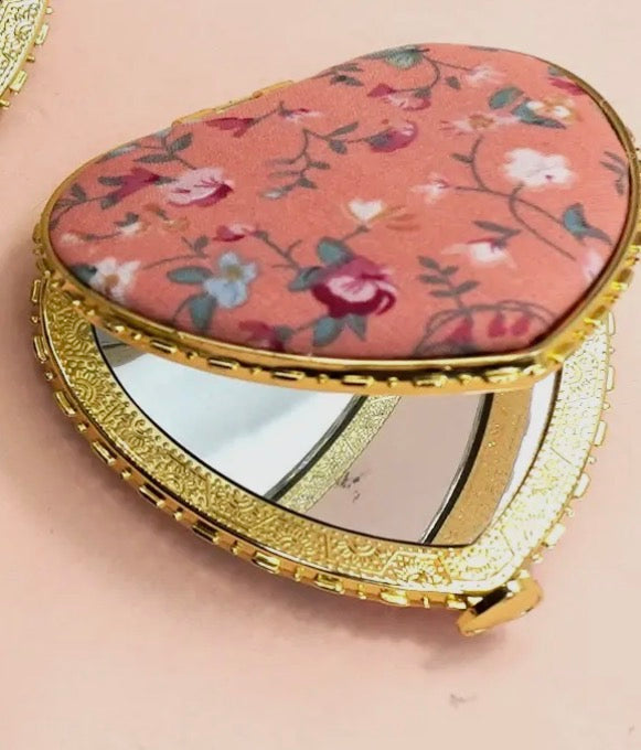 Compact mirror with floral lid on a pink background
